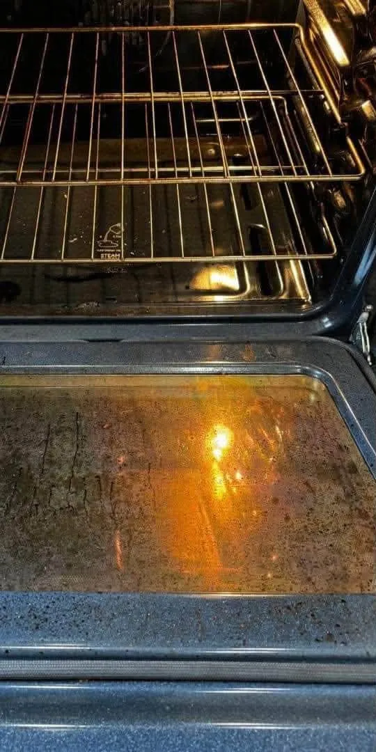 Oven door glass before cleaning, brown and spotted with grease